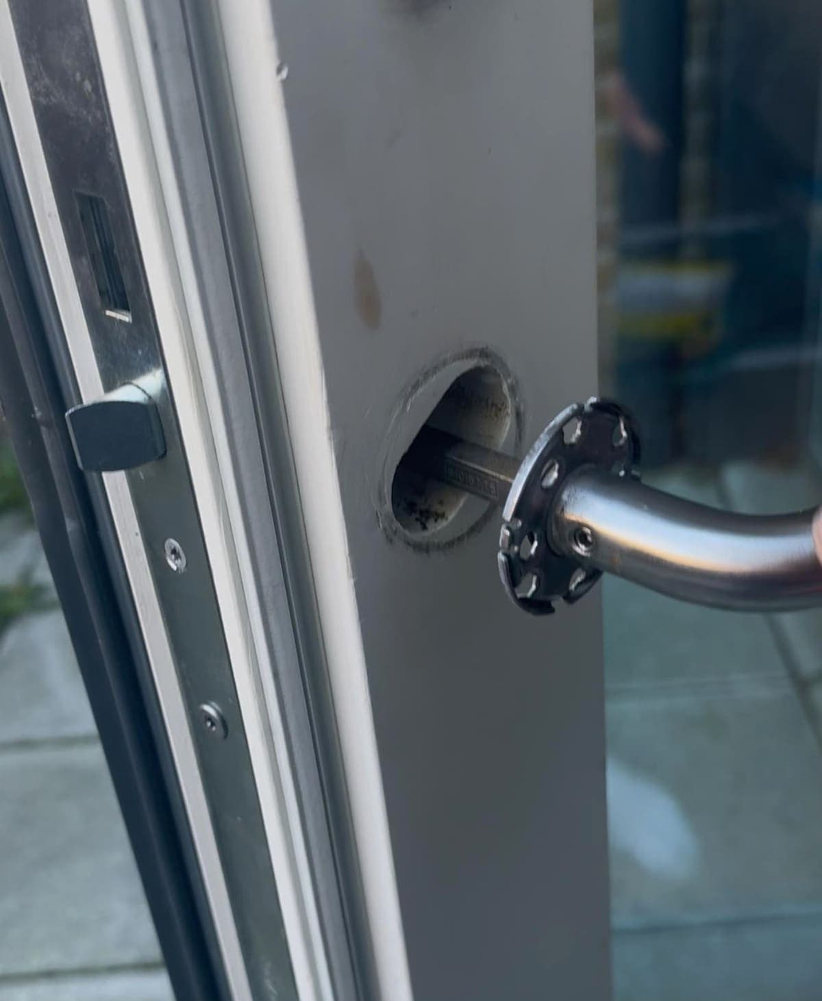 A lever handle drawn away from an aluminium door, exposing the lock beneath