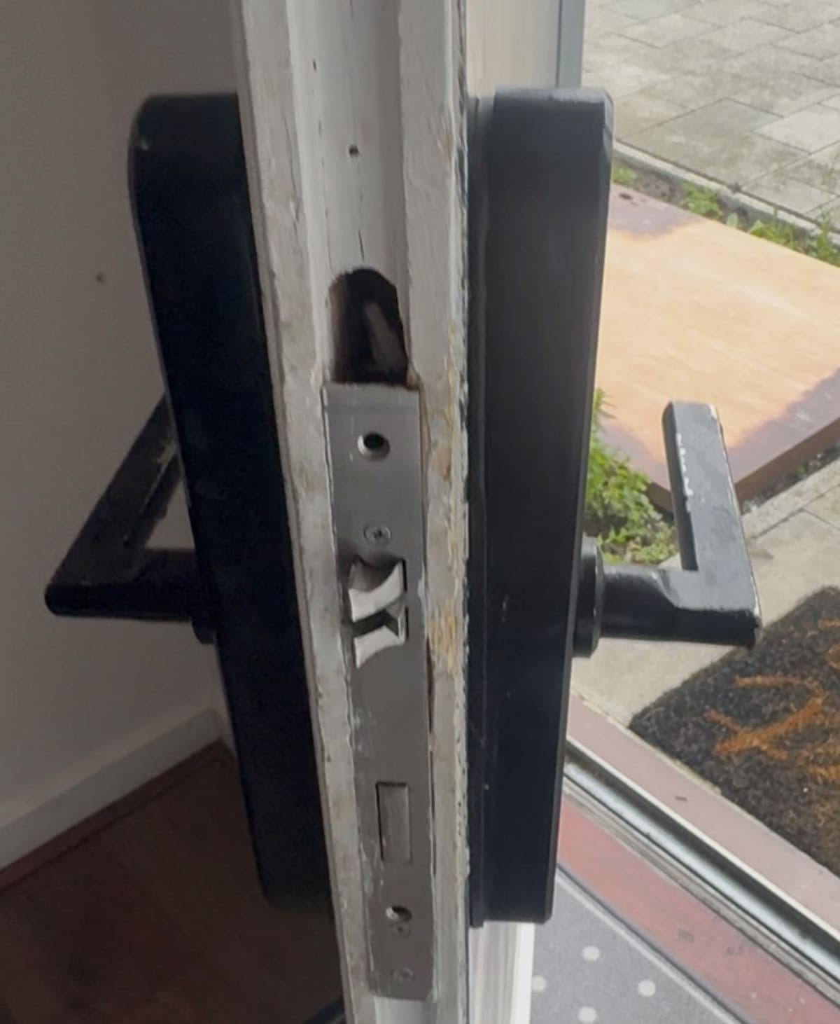 A lock faceplate and black lever handles on the edge of an open door
