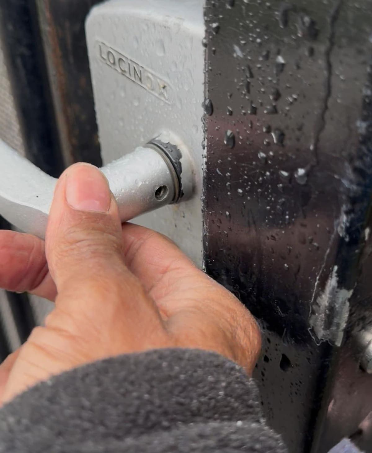 A close-up of a hand operating the lever of a metal gate lock