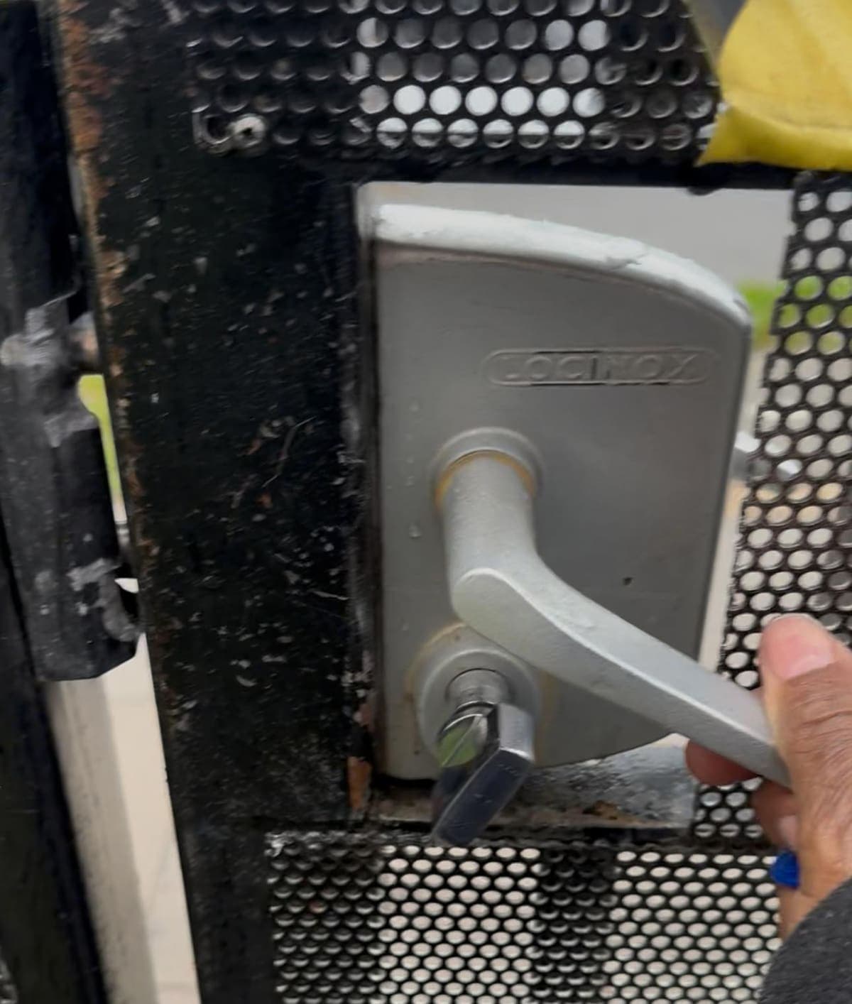 A hand on the lever of a Locinox lock fitted to a perforated metal security gate